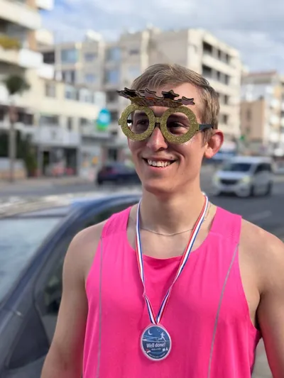 A runner in a pink vest wearing gold novelty glasses, finisher medal round his neck.