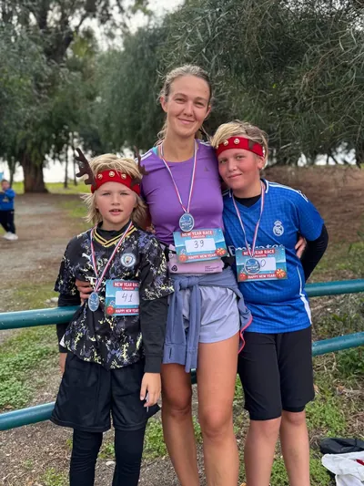 A woman and two children with race bibs and finisher medals by the seafront railing.