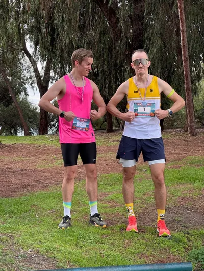 Two runners standing on the grass, showing their race bibs.