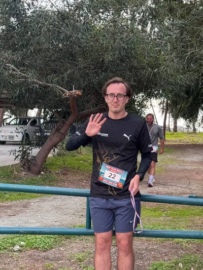 A runner waving to the camera, finisher medal round his neck.